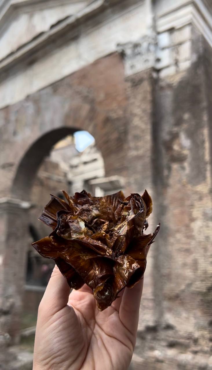 Crispy fried artichoke held up in front of the ancient brick arches of a Roman ruin