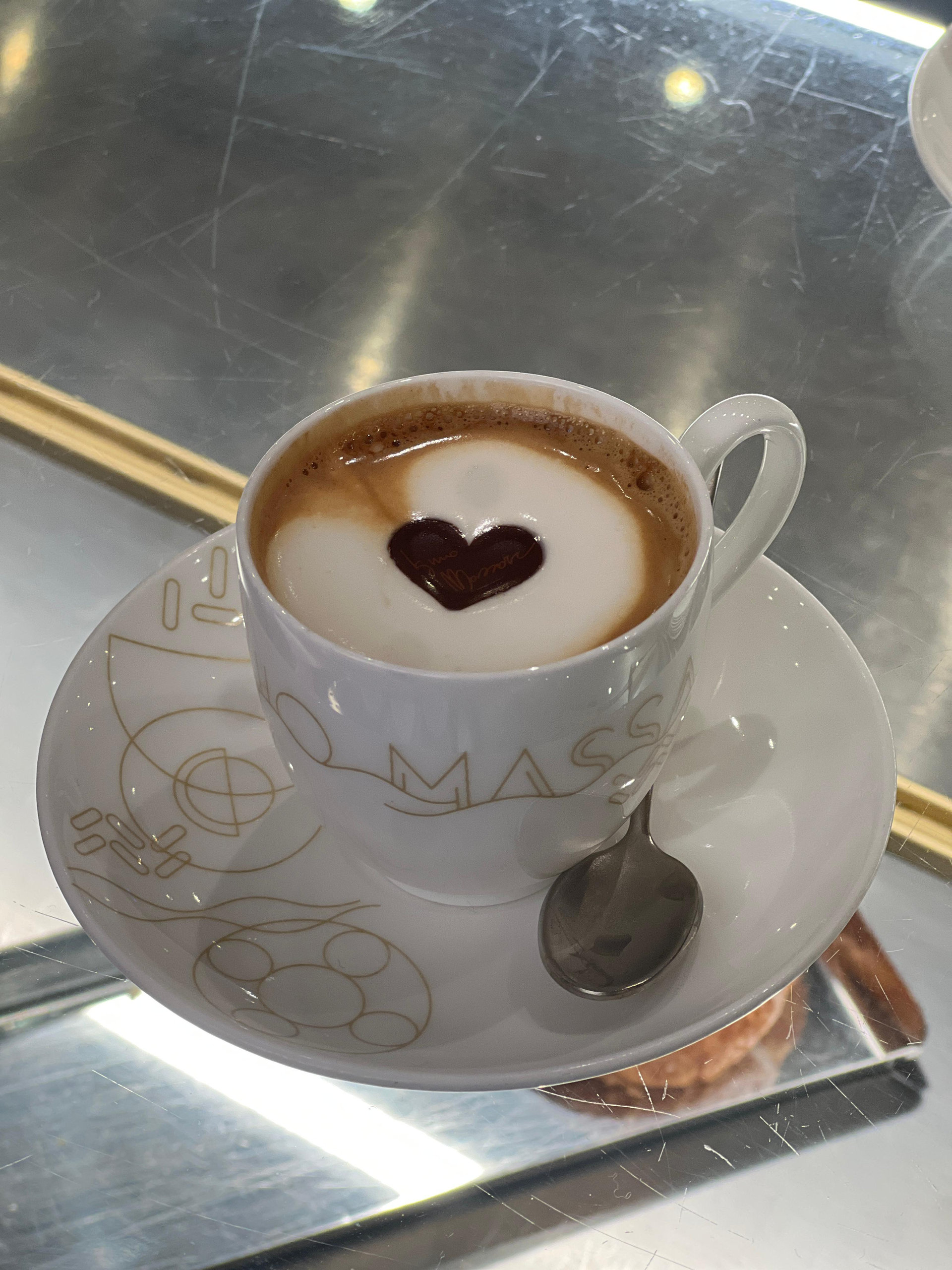 Cappuccino with a chocolate heart on the foam, in a white cup on a mirrored counter