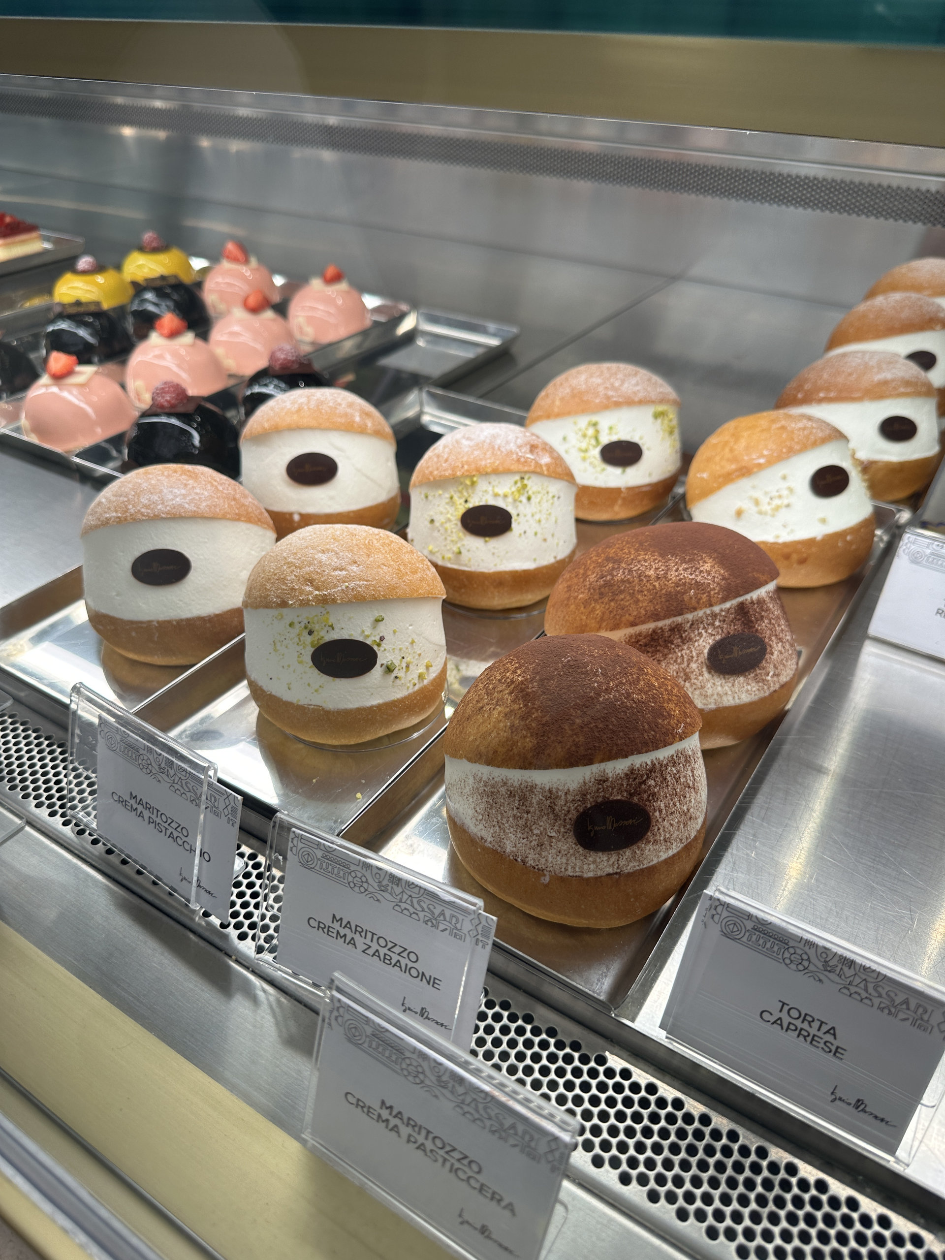 Display case of maritozzi, cream-filled sweet buns, and colourful pastries