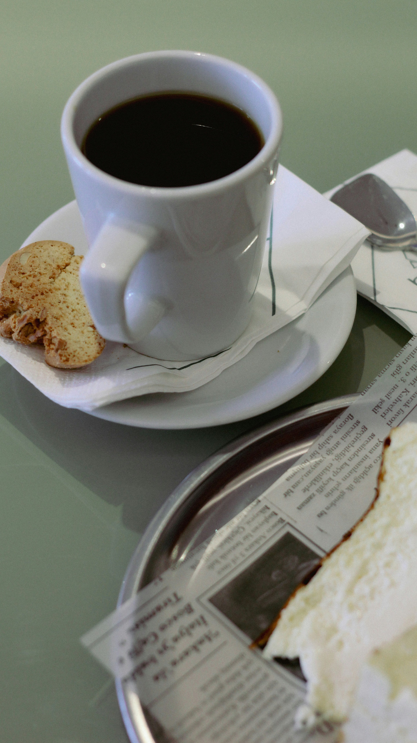 Espresso with almond biscotti beside a slice of cake on a tray lined with newspaper