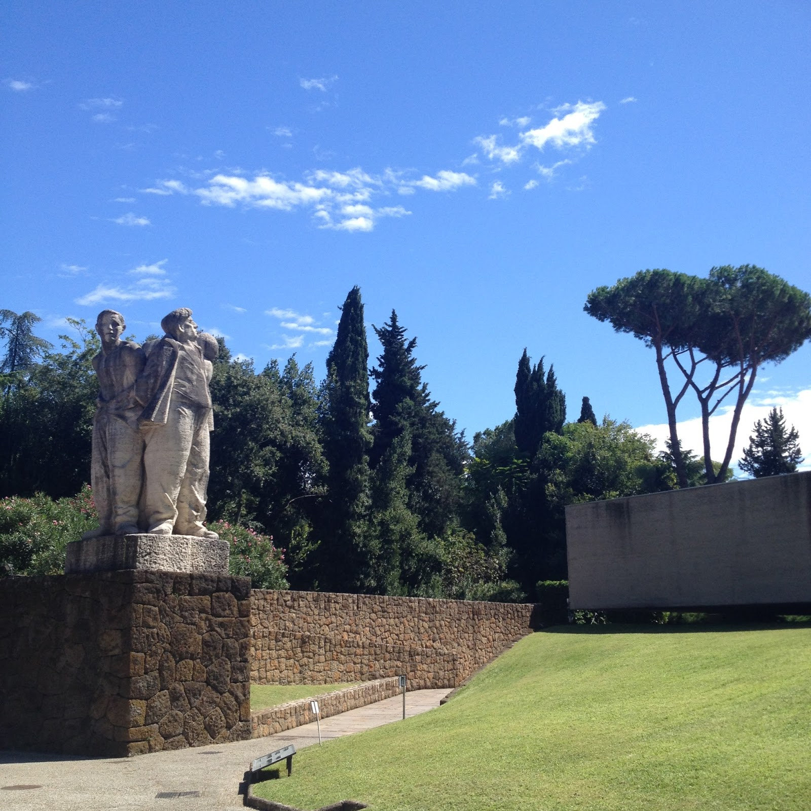 Stone sculpture group on a wall beside a memorial lawn under a blue sky