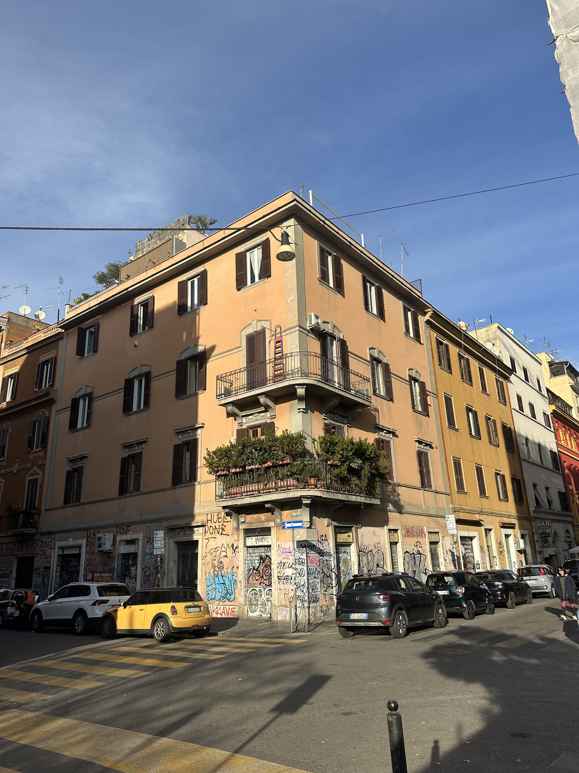 Ochre corner building with balconies and graffiti-covered ground floor on a Roman street