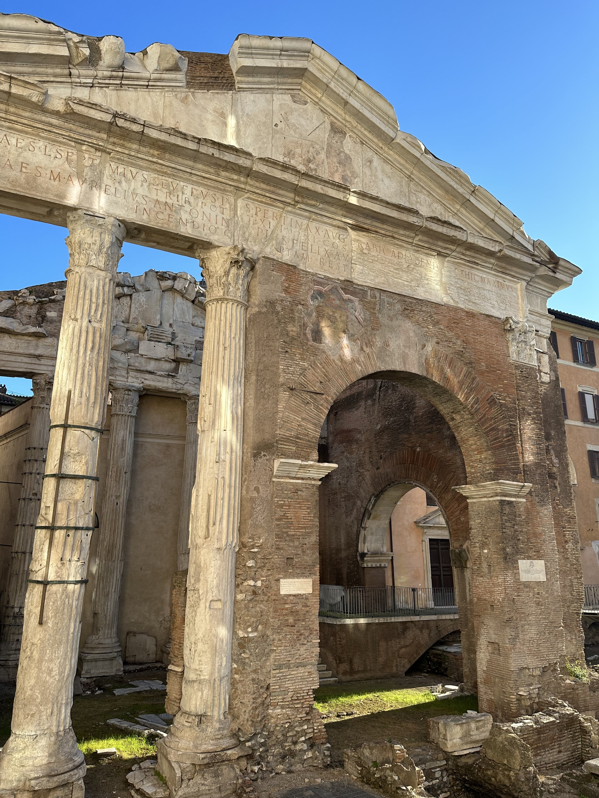 Ancient Roman portico with tall columns and a brick arch under a blue sky