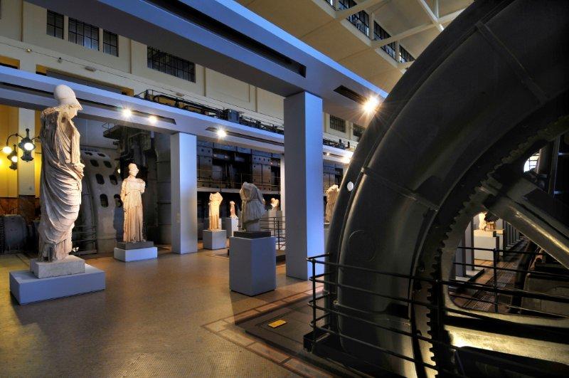 Classical statues in the engine hall, with the edge of a huge toothed black flywheel on the right