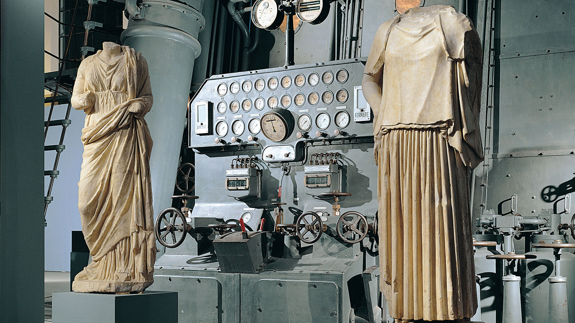 Two draped marble statues flanking a vintage control board with gauges and handwheels