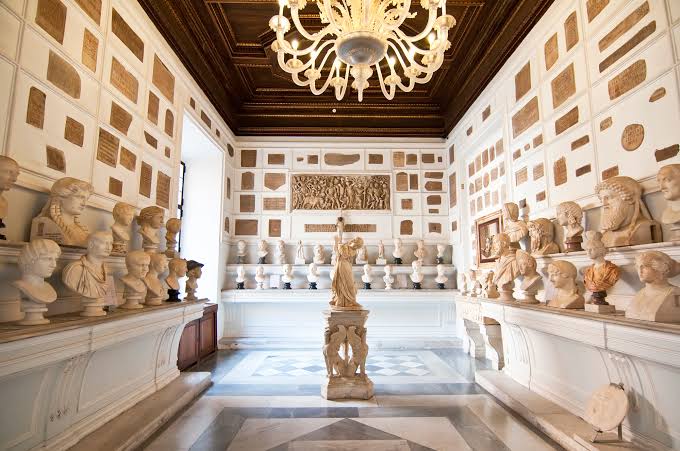 Museum hall lined with Roman portrait busts, a chandelier and inscribed plaques on the walls