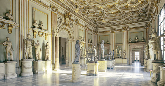 Grand hall with a coffered ceiling and classical statues on pedestals over a marble floor