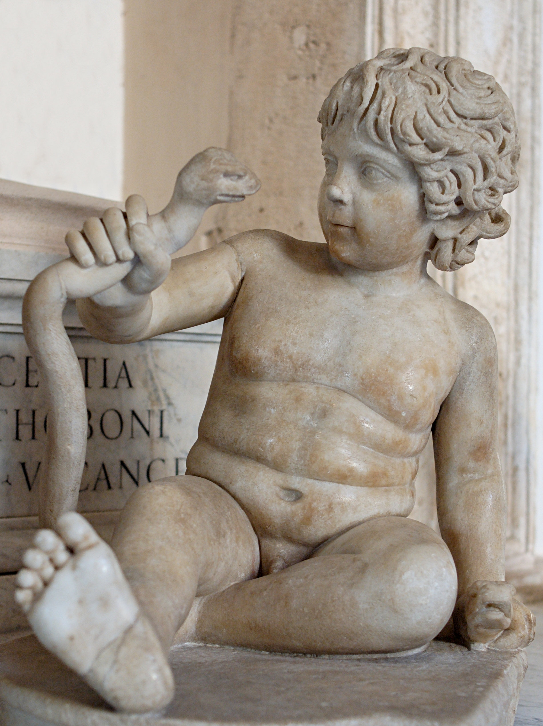 Ancient marble statue of a curly-haired child holding a snake