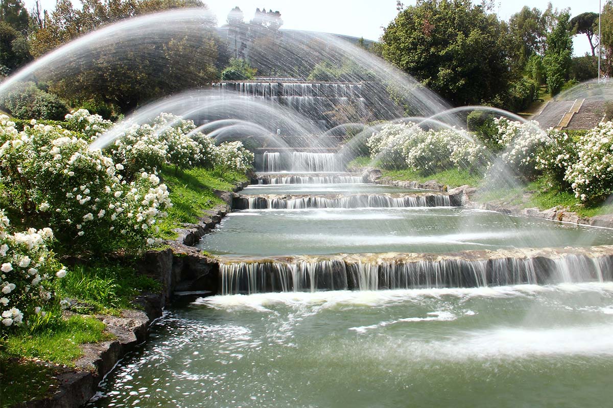 Terraced cascade fountain with arching jets of water among white flowering shrubs