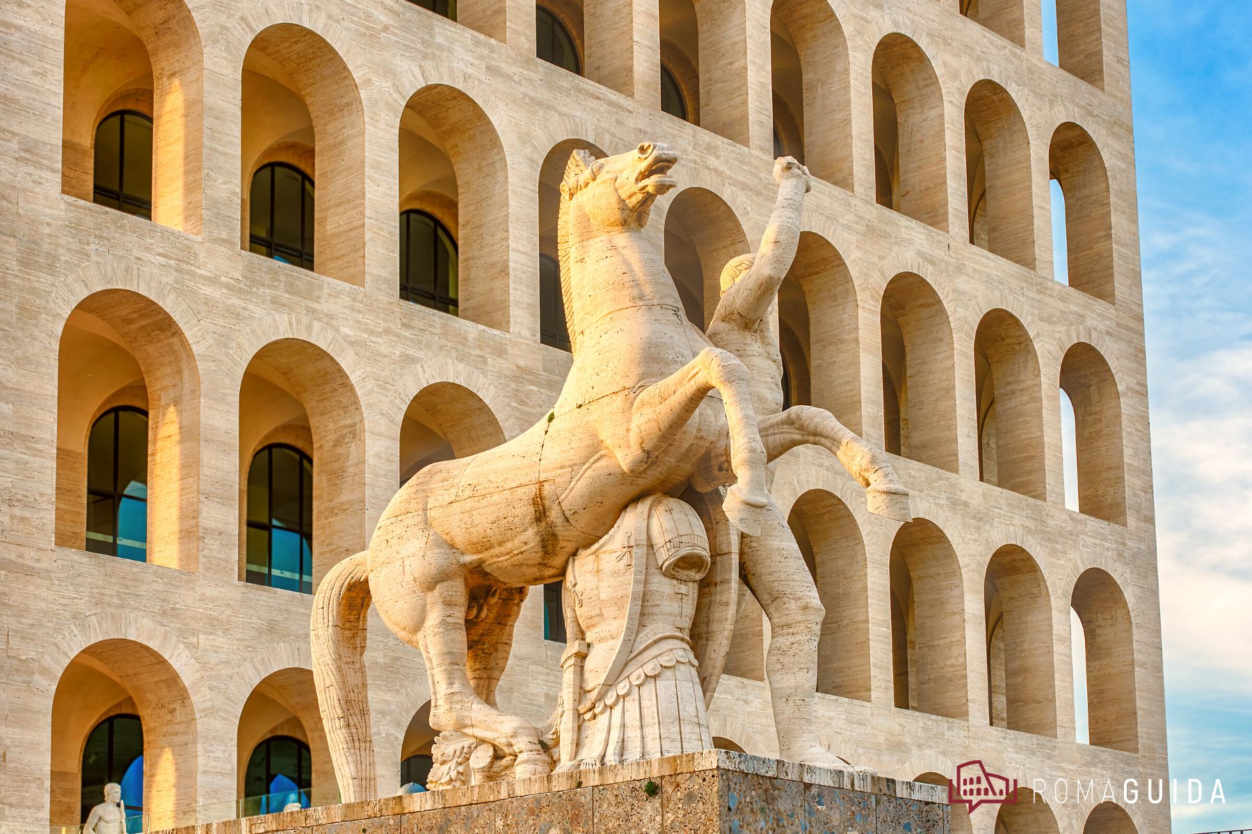 Marble horse-tamer statue in front of the arched travertine facade of a rationalist building
