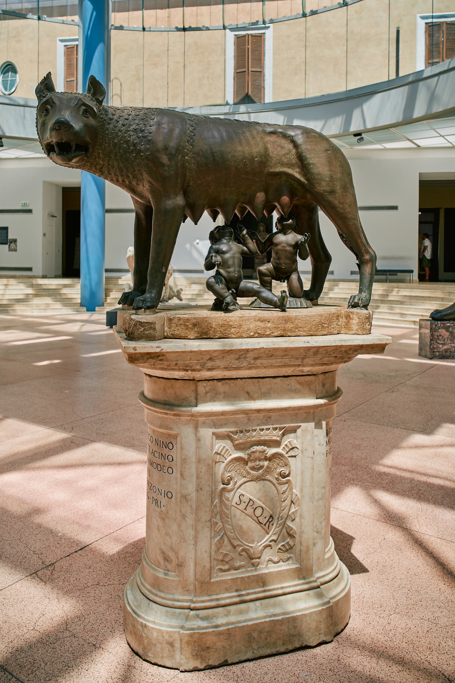 Bronze she-wolf suckling the twins Romulus and Remus on a marble pedestal in a bright atrium
