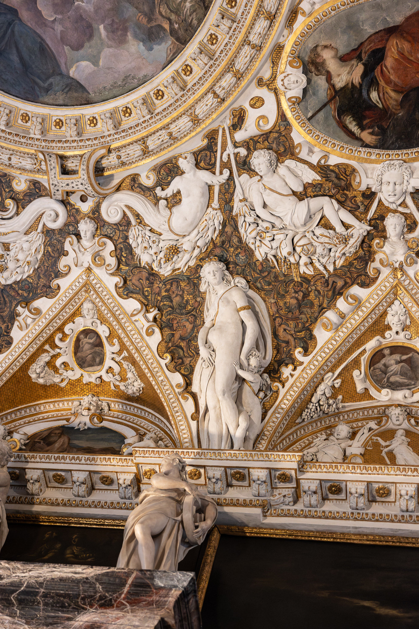 Ornate gilded and stuccoed wall with white sculpted figures and painted ceiling panels in a Venetian palace