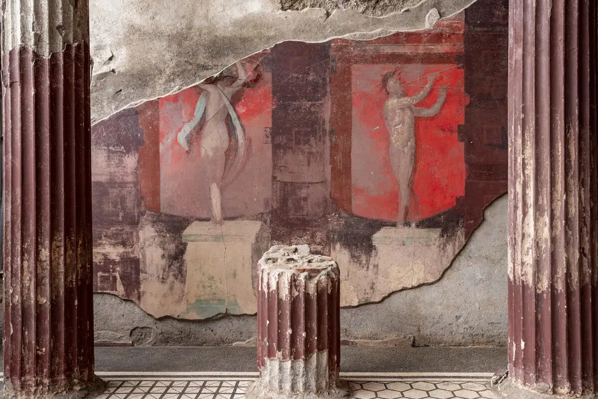 Fresco of dancing figures on a red wall between deep-red fluted columns in an ancient villa