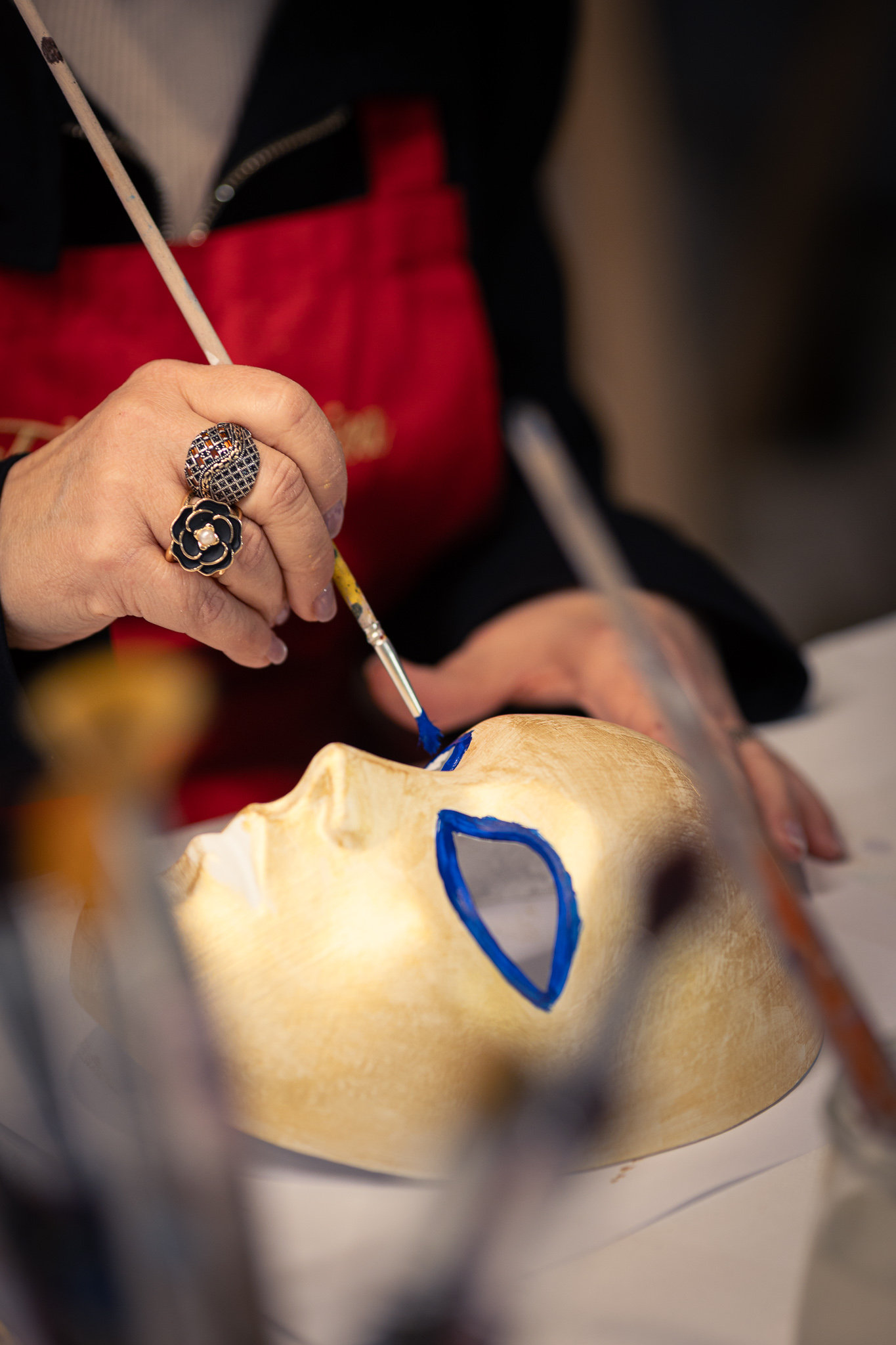 Hand with a fine brush painting a blue outline on a gold mask