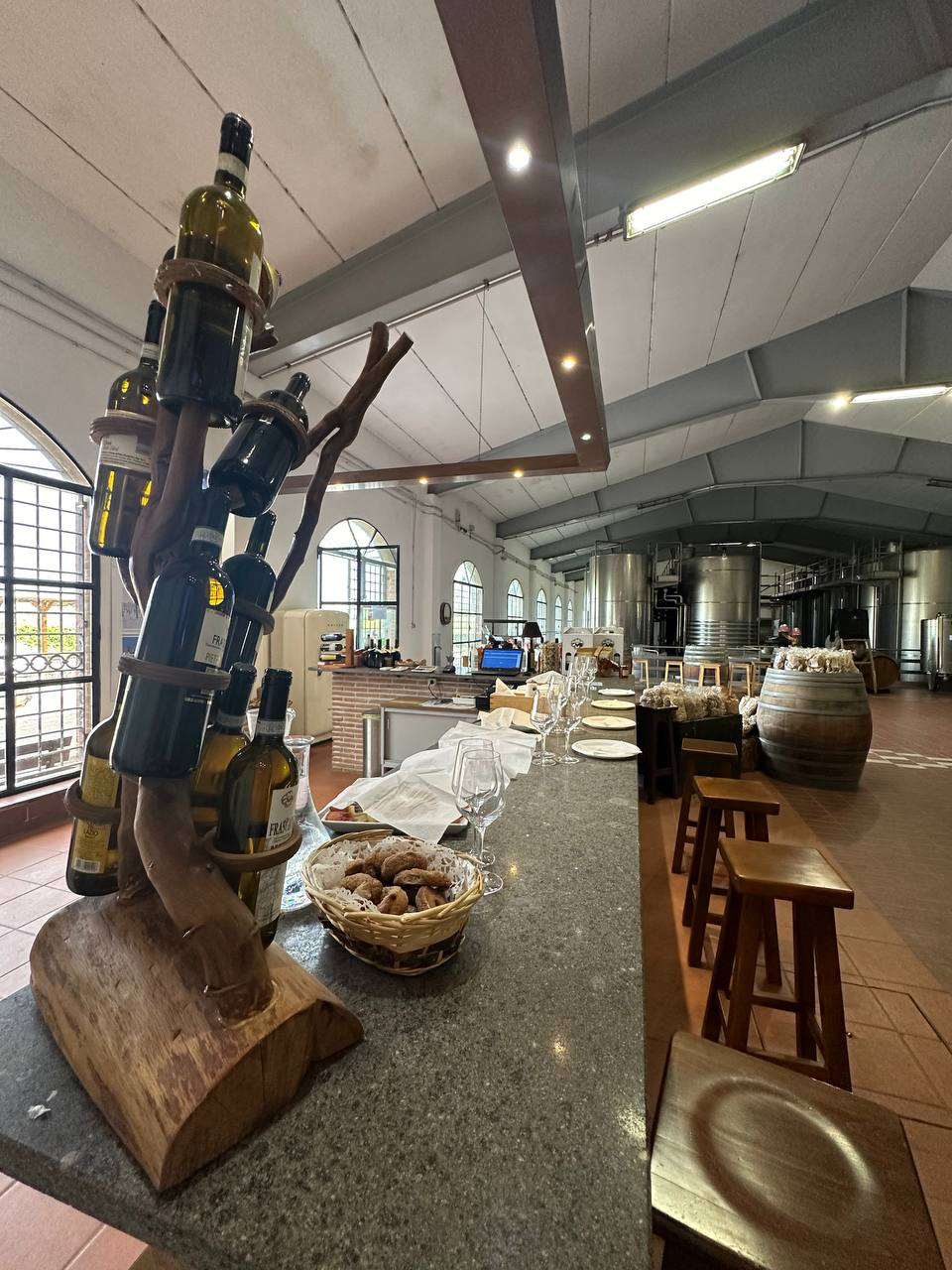 Winery tasting counter with a wine-bottle display, bread basket and steel tanks behind