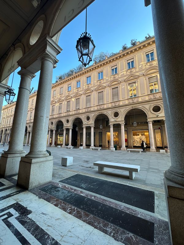 Elegant arcaded courtyard with marble columns, a hanging lantern and stone benches in Turin