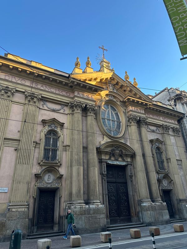 Baroque church facade with an oval window and carved doors on a Turin street