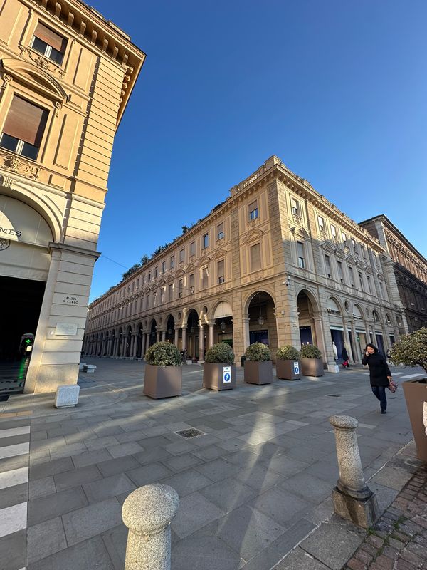 Ochre arcaded buildings around a paved square under a deep blue sky in Turin