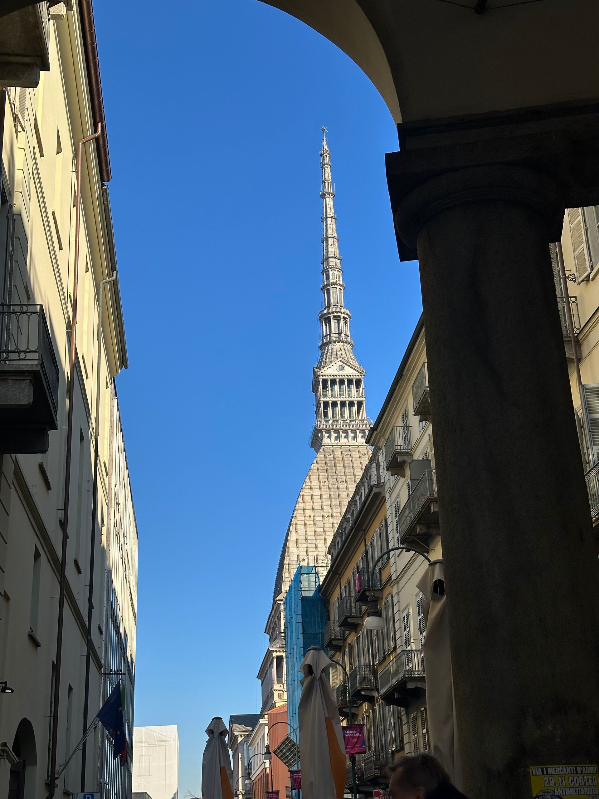 Mole Antonelliana spire glimpsed between arcade columns and buildings on a Turin street