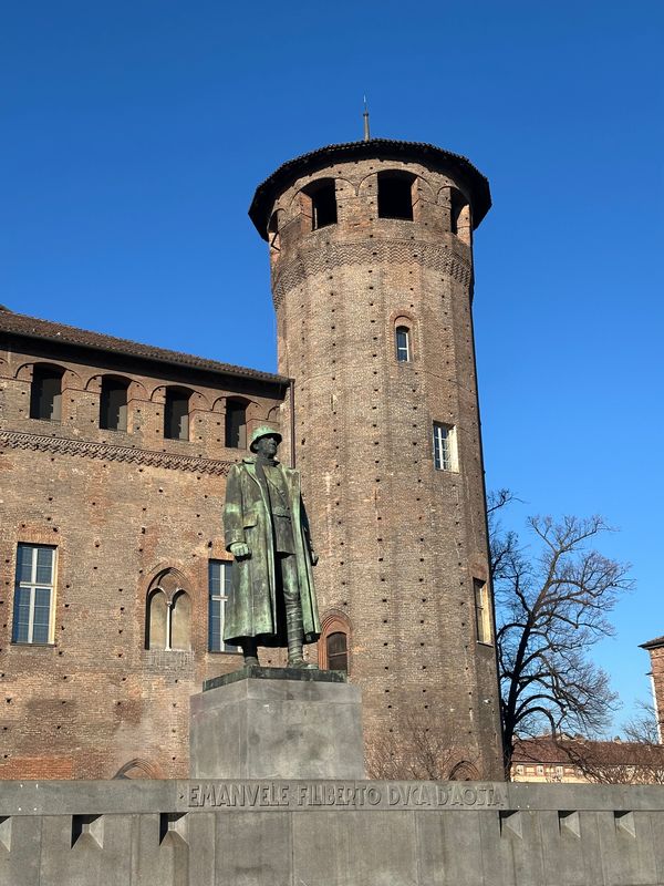 Bronze statue of a soldier in front of a brick tower of a Turin palace