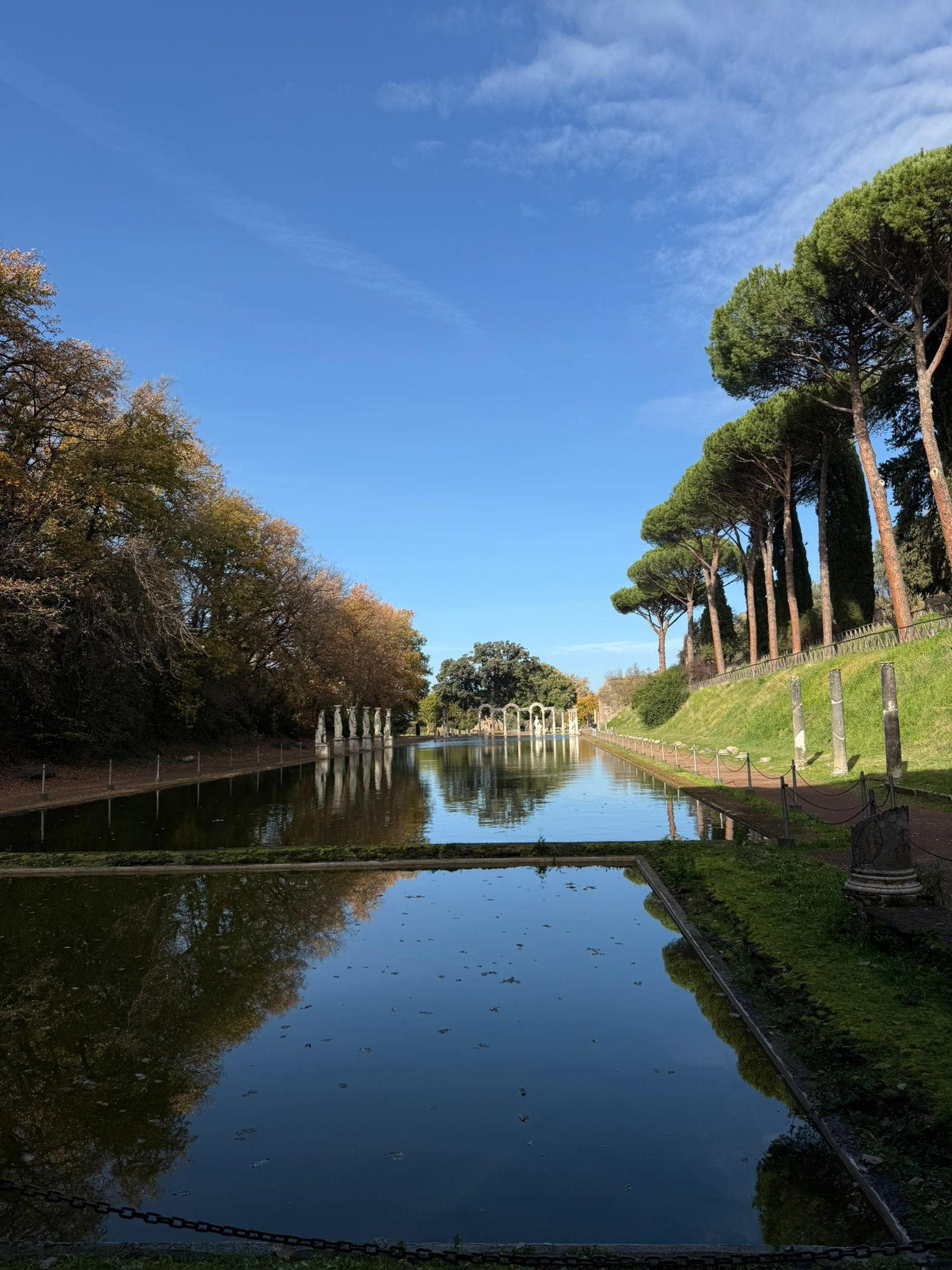 Long reflecting canal lined with autumn trees and umbrella pines at Hadrian's Villa