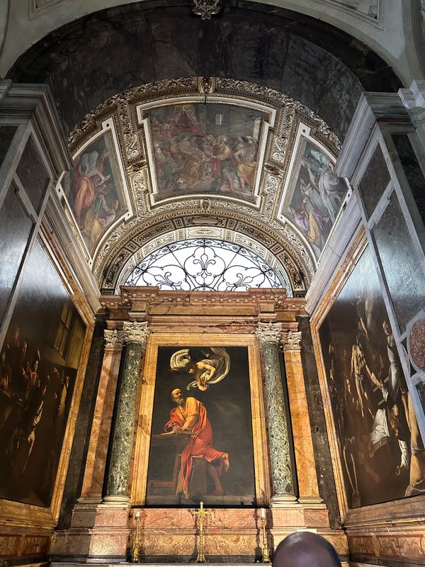 Caravaggio's Saint Matthew and the Angel above an altar in a frescoed chapel
