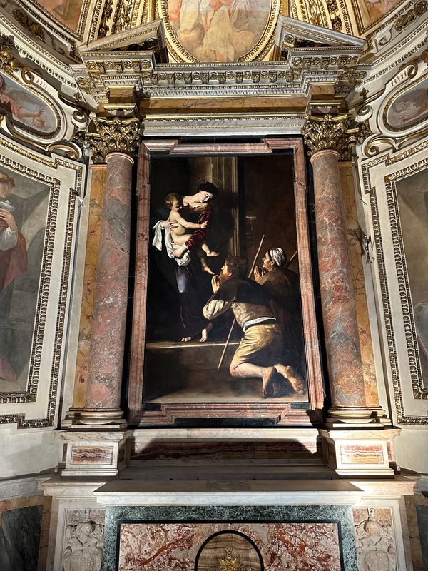 Caravaggio's altarpiece of the Madonna with pilgrims between marble columns in a side chapel