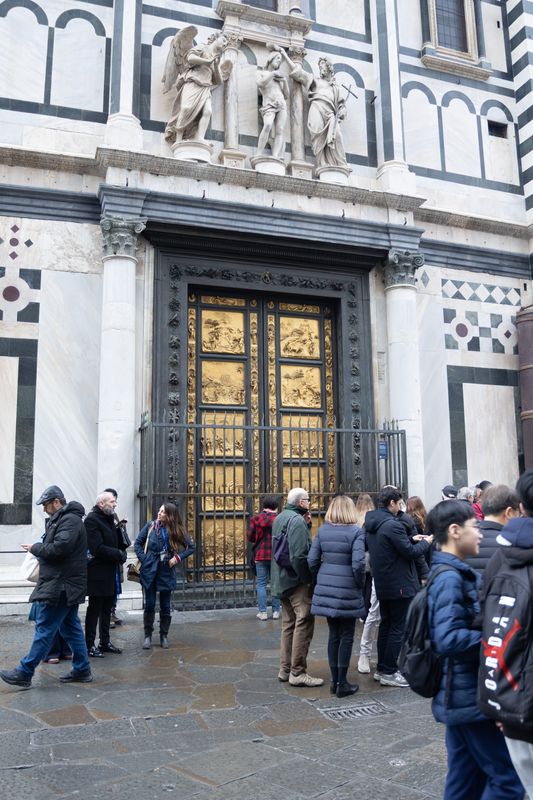 Visitors queuing outside the Baptistery's gilded bronze doors in a marble wall