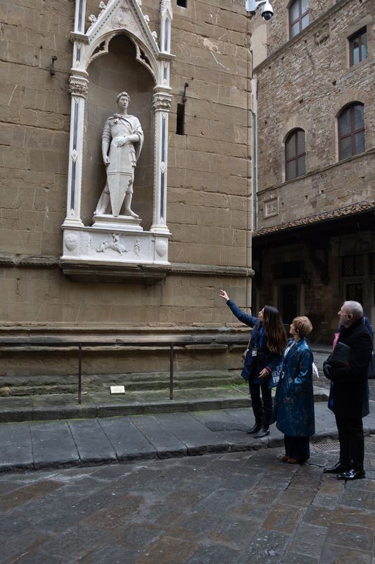 Guide pointing up at a statue of a knight in a Gothic niche on the outer wall of Orsanmichele