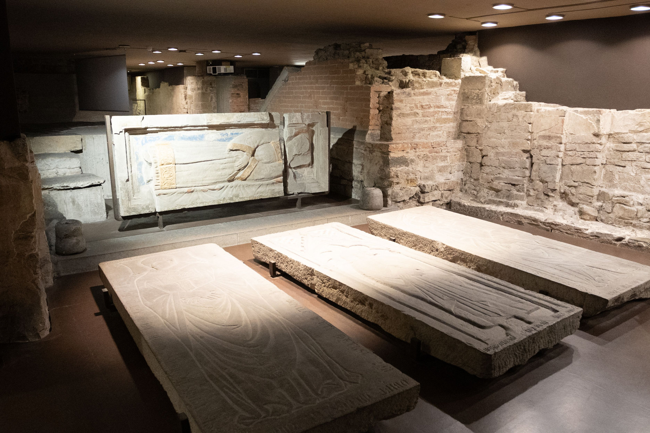 Carved stone tomb slabs and ancient brick walls in the lit excavations beneath the cathedral