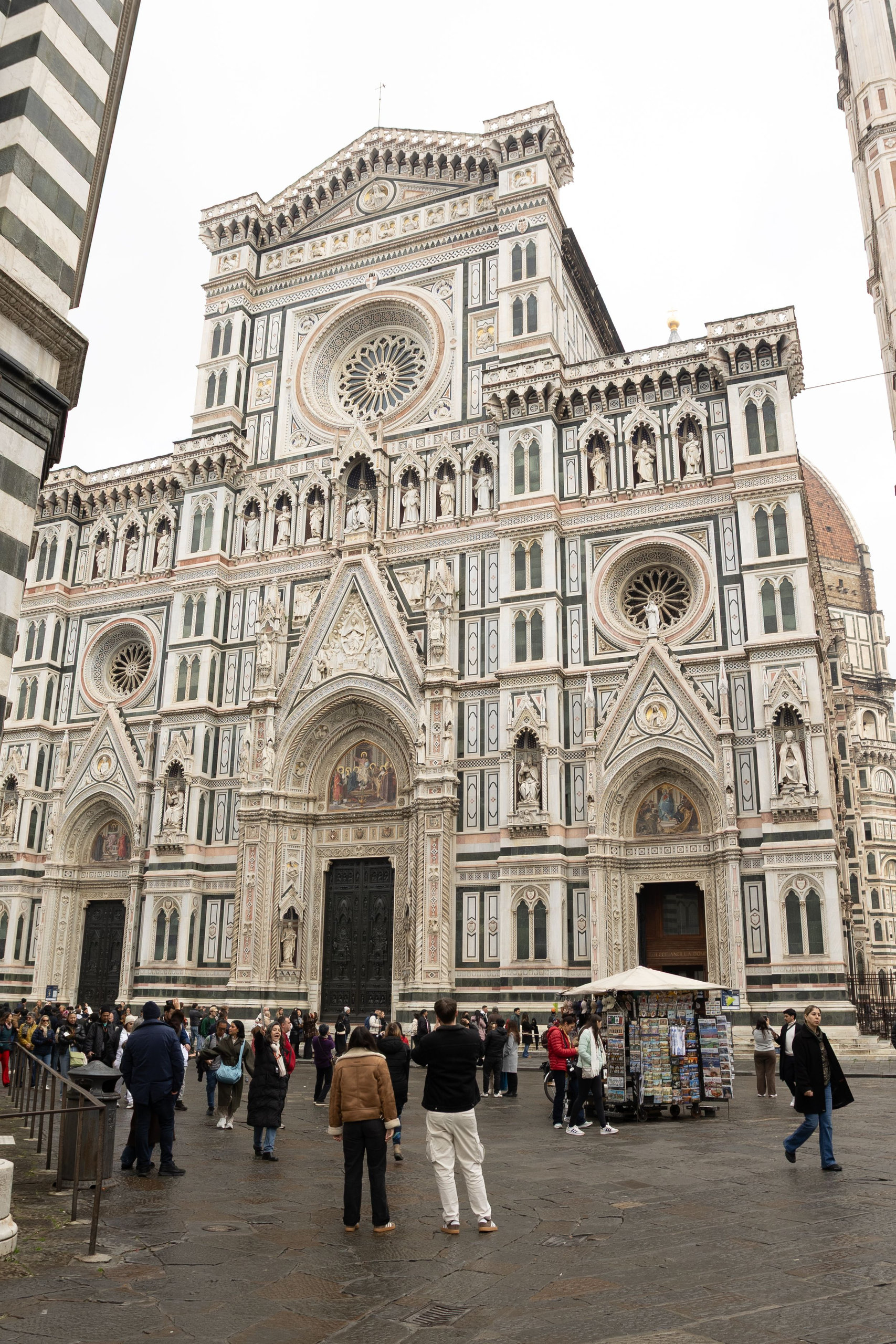Pink, green and white marble facade of Florence Cathedral with visitors in the square