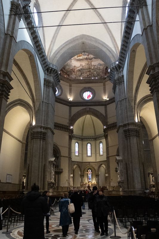 Nave of Florence Cathedral with grey stone piers and the painted dome in the distance
