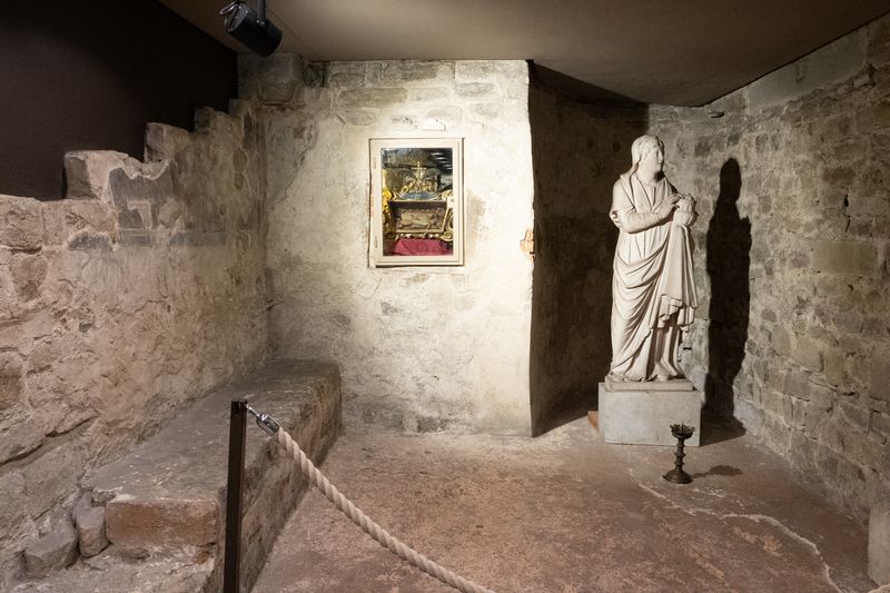 Marble statue of a robed woman beside a small reliquary in a stone crypt chamber