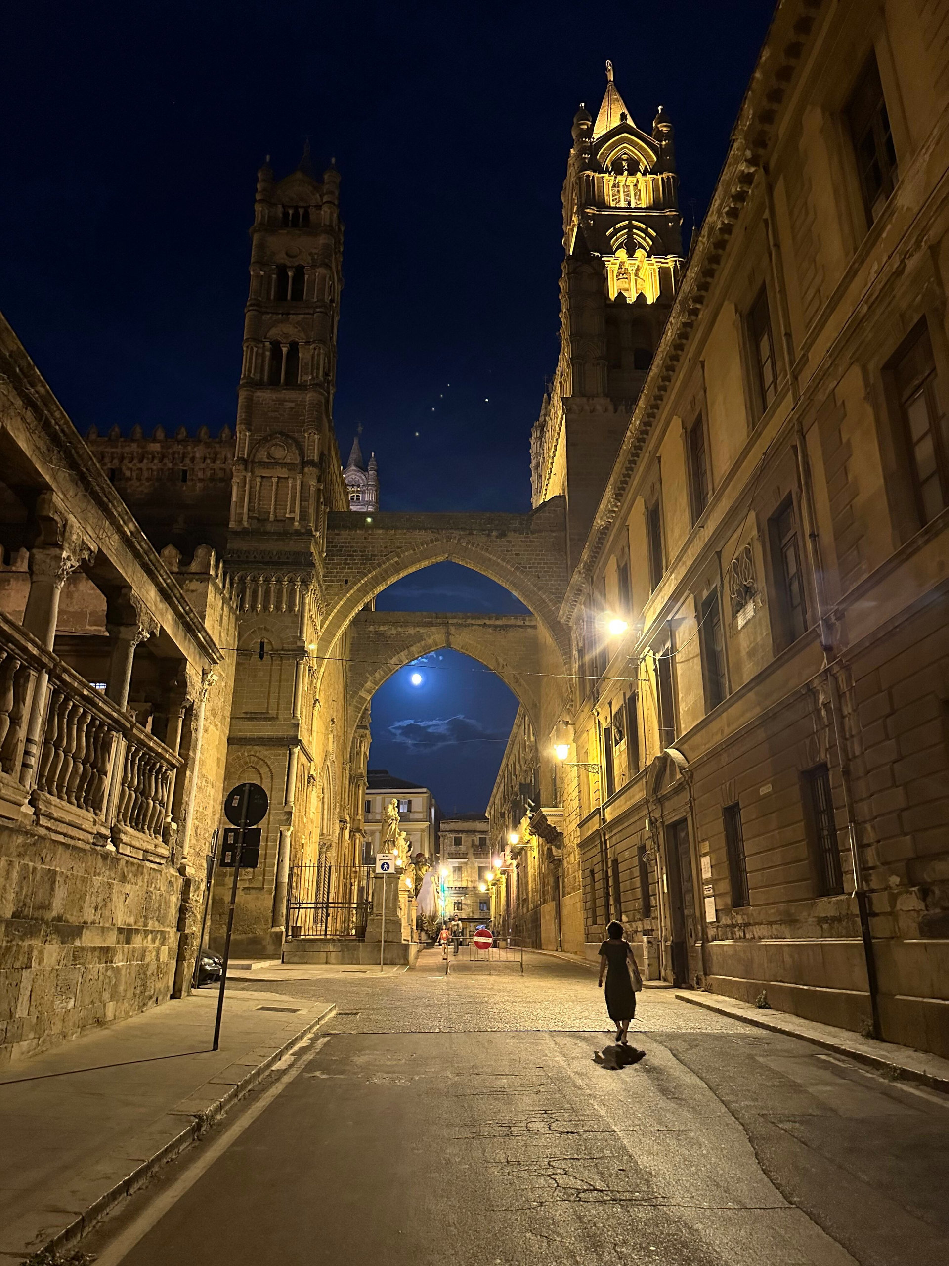 Cathedral towers and a stone archway lit up on a quiet street at night