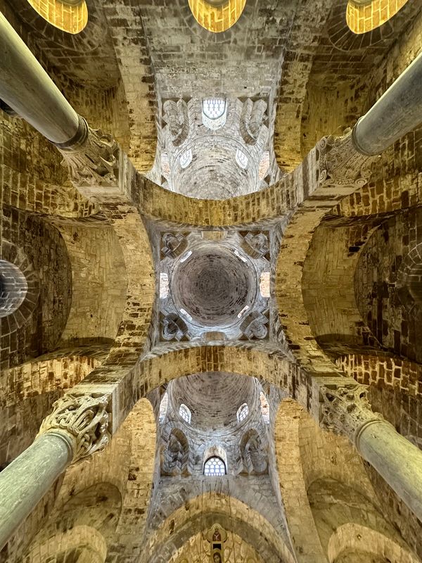 Looking up at a dome and stone arches supported by slender columns inside a Norman church