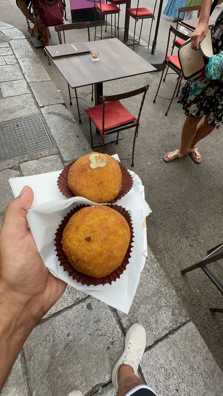 Two arancini on paper cups held in a hand beside a street table