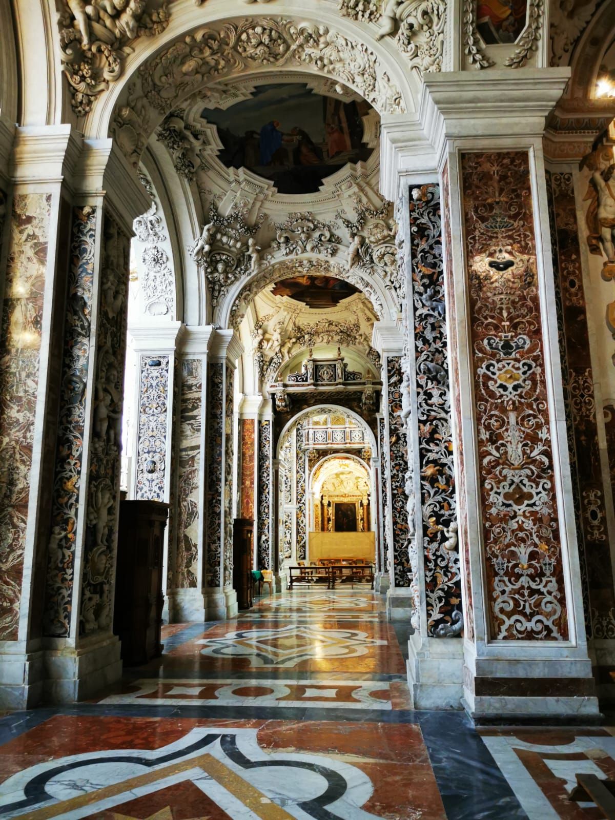 Baroque church aisle with marble inlaid columns and a patterned mosaic floor