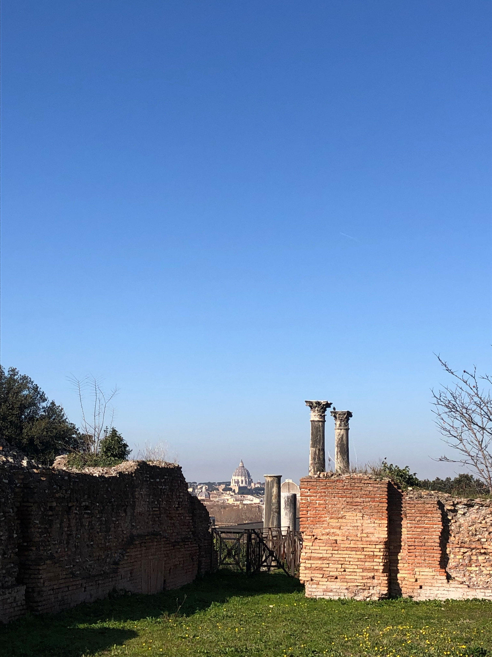 Two ancient columns and brick walls with the dome of St Peter's in the distance