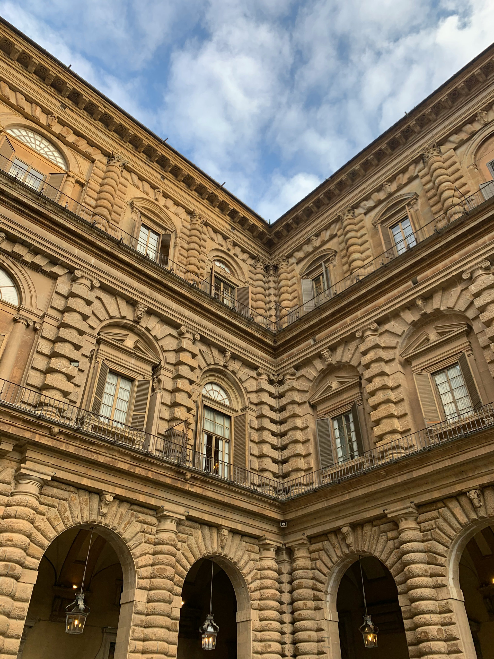 Rusticated stone walls and arched windows of the Pitti Palace courtyard against a cloudy sky