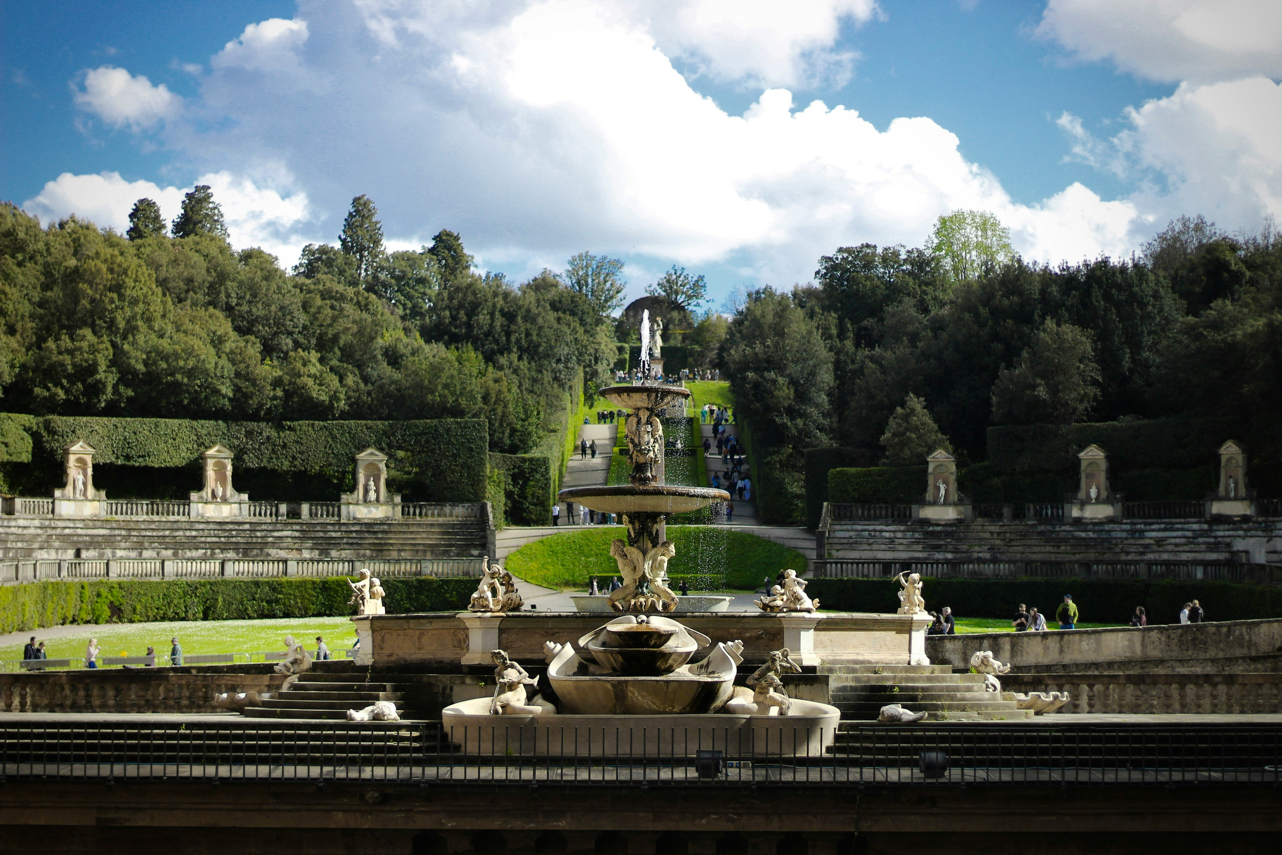 Fountain with sculpted figures at the centre of a garden amphitheatre, framed by tall green trees