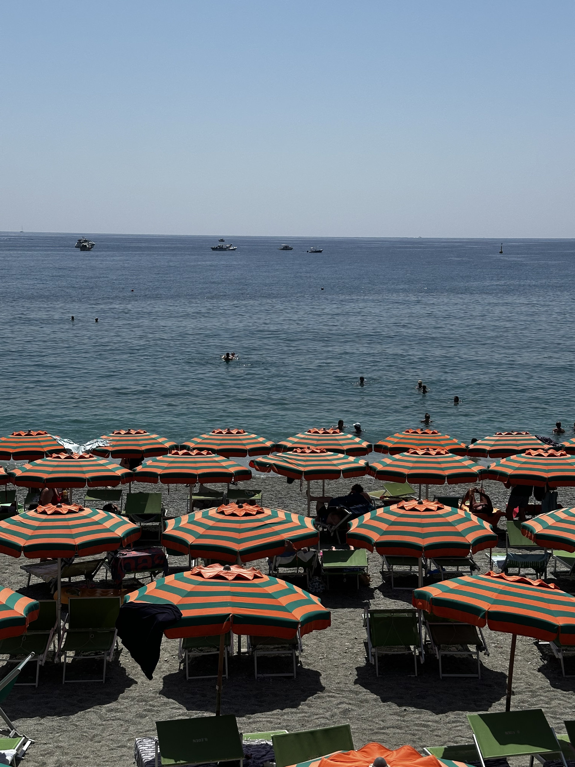 Rows of orange-and-green striped beach umbrellas and sun loungers facing a calm sea