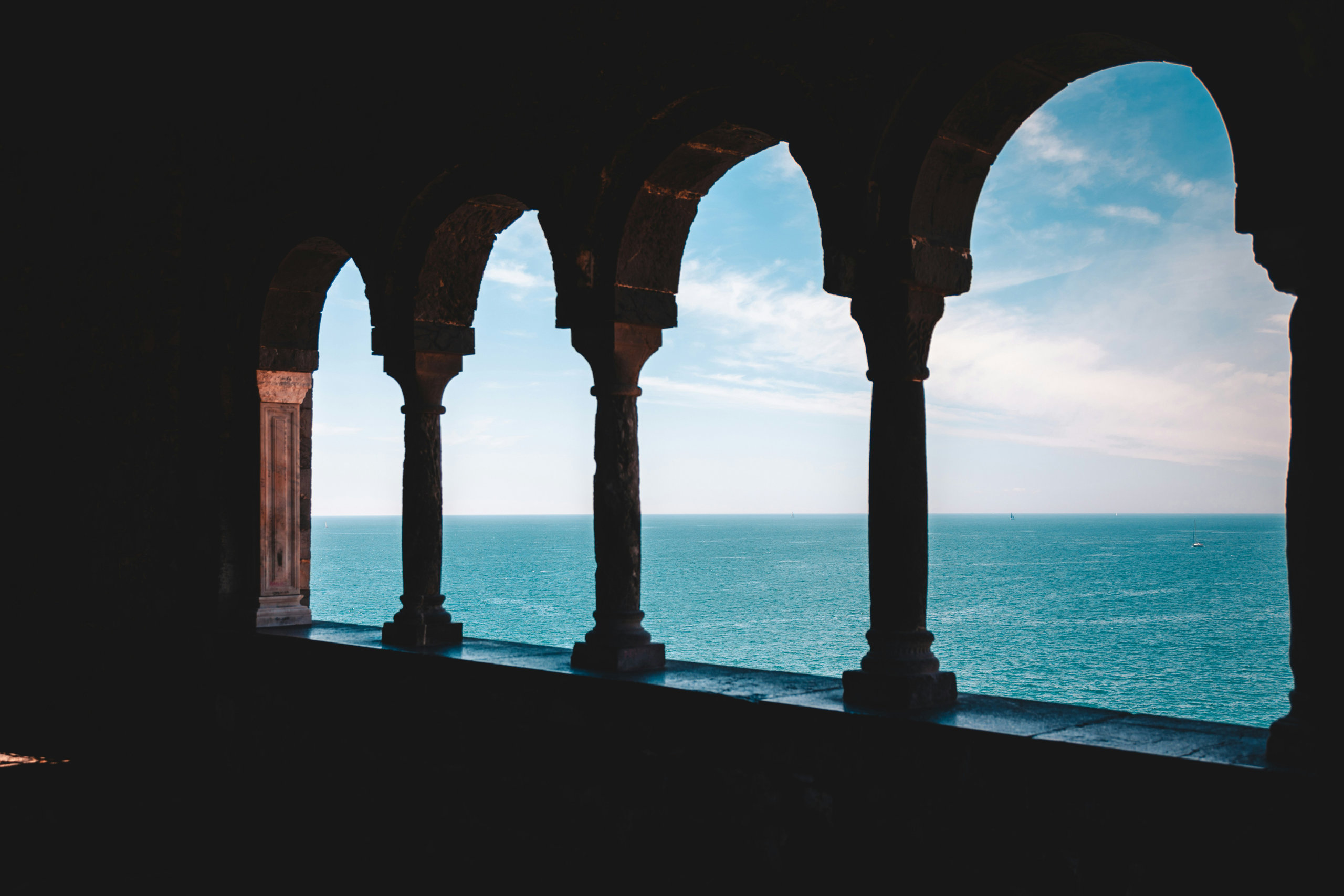 Silhouetted stone arches and columns opening onto a bright turquoise sea