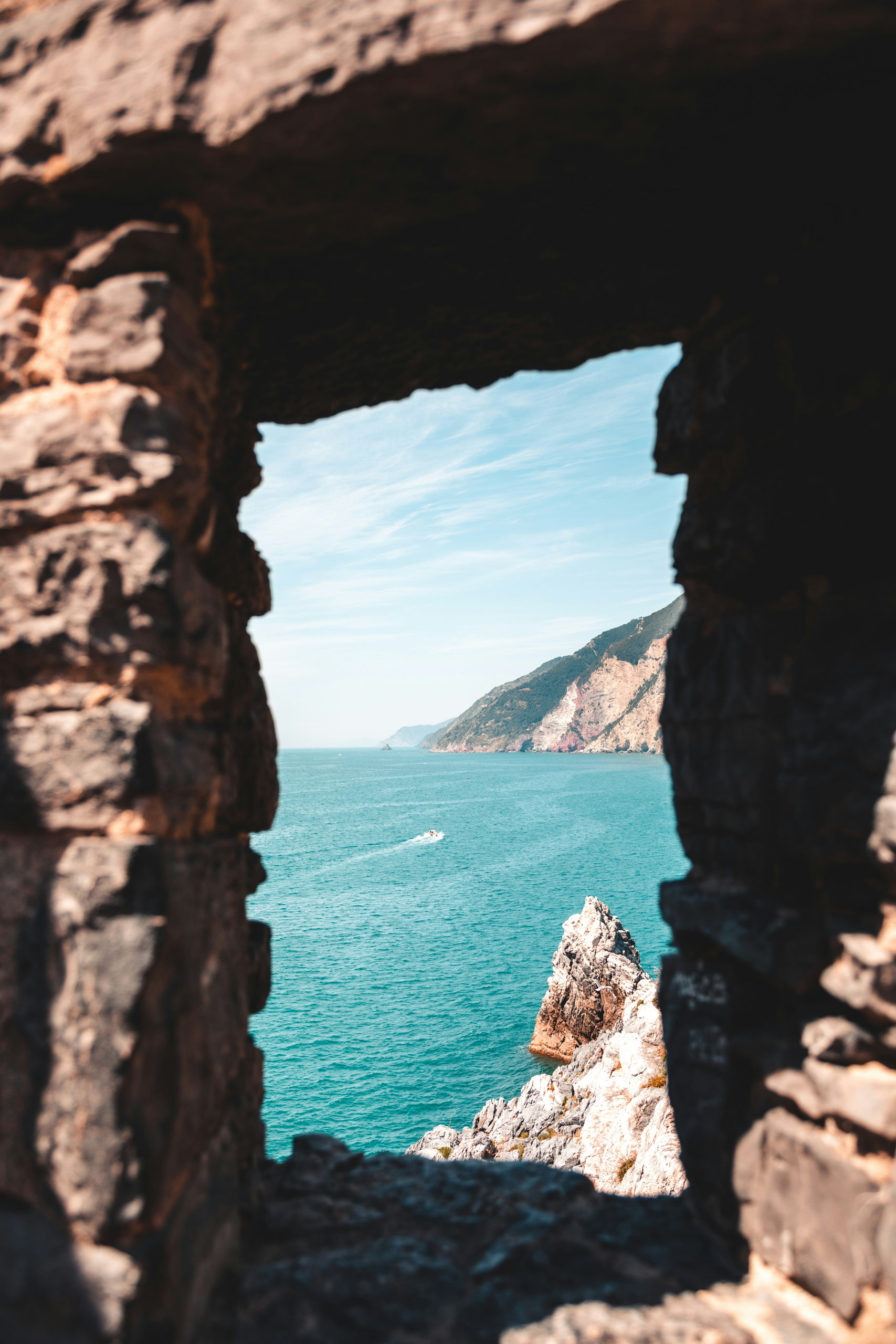Rugged stone window framing turquoise water and a rocky cliff coastline