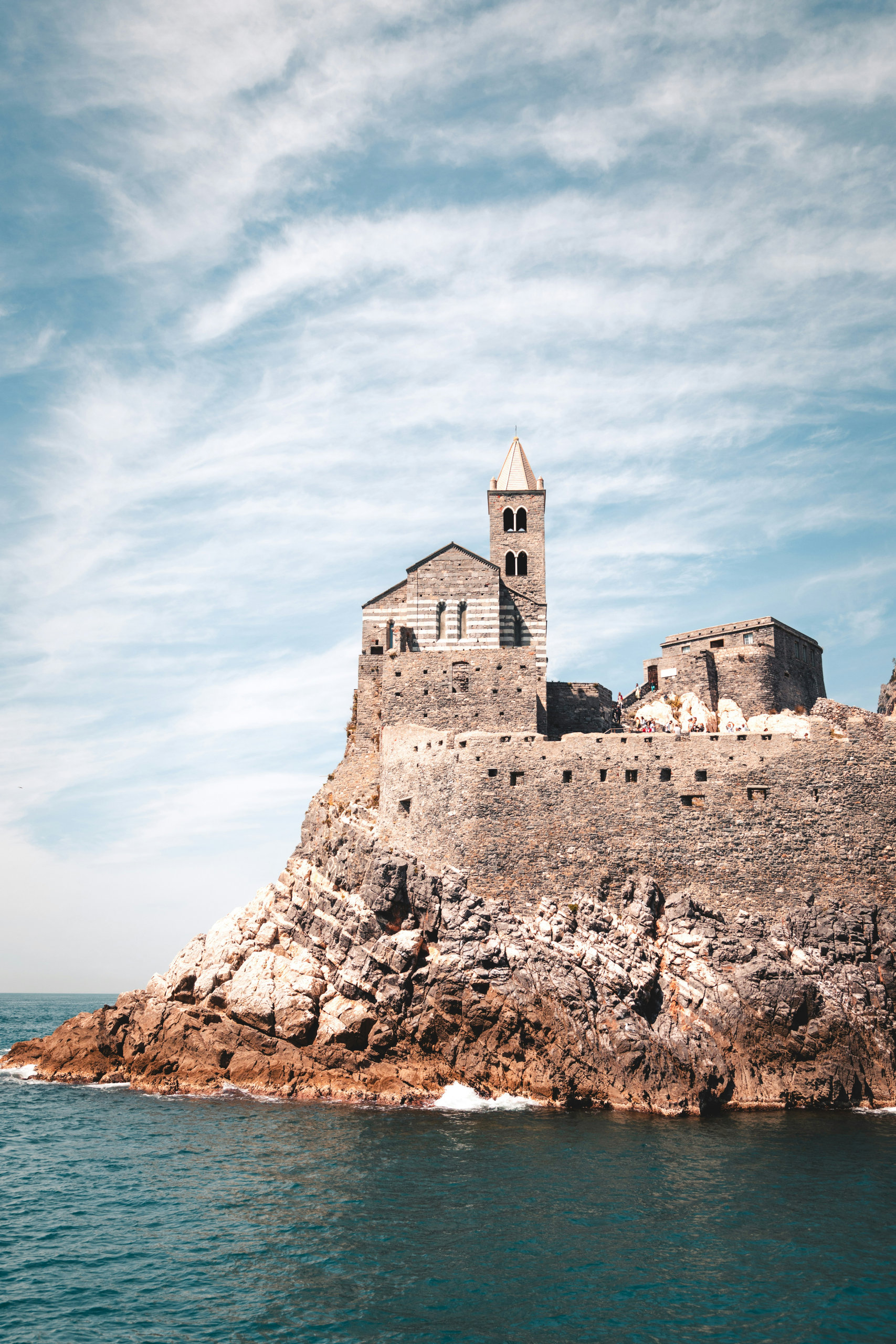 Medieval striped-stone church with a bell tower perched on a rocky headland above the sea