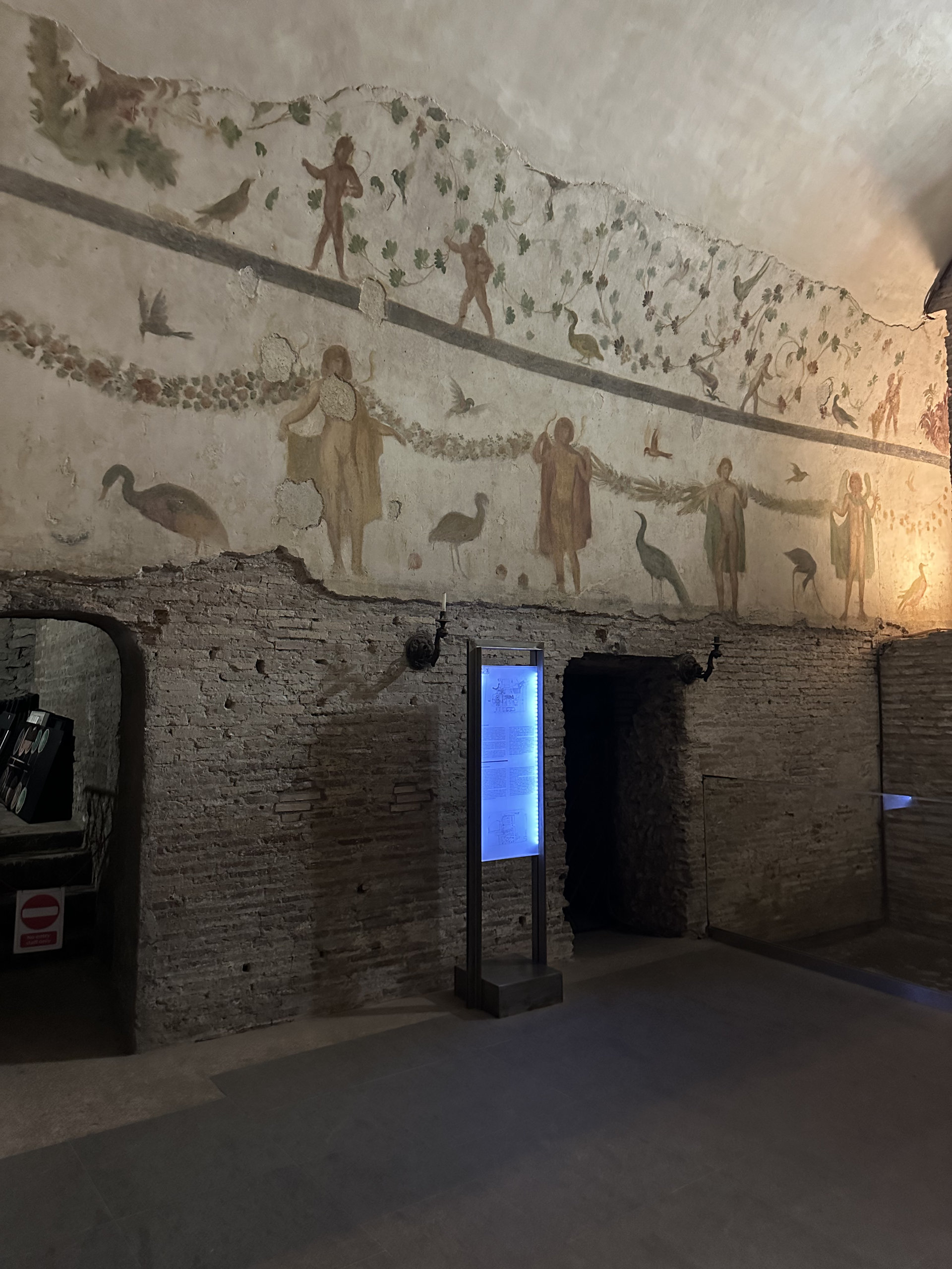Ancient wall fresco of cherubs, birds and garlands above a brick archway in an underground room