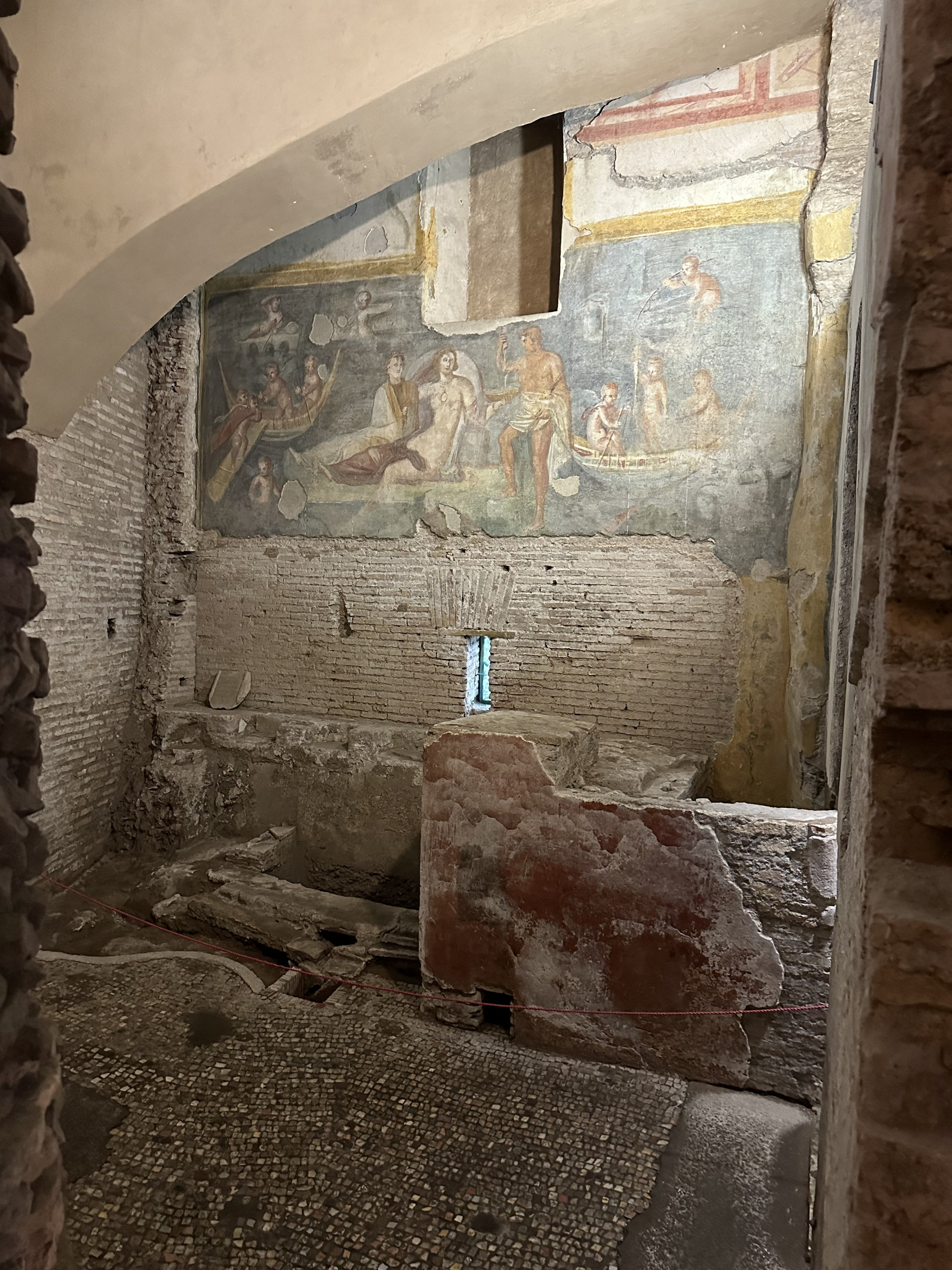 Faded Roman wall painting of boats and figures at sea, with a small window below