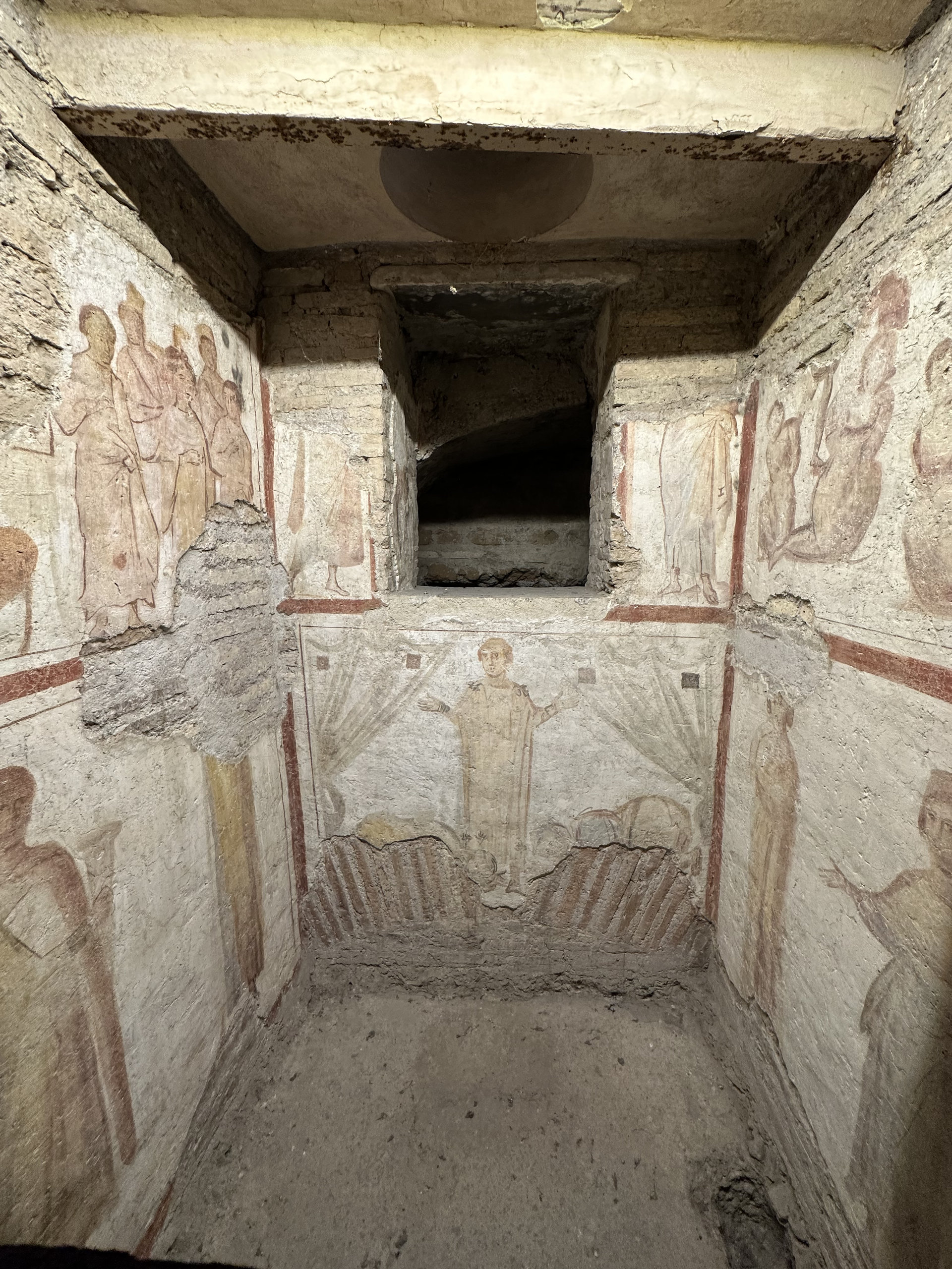 Narrow burial chamber with early Christian fresco figures on the walls and an arched niche