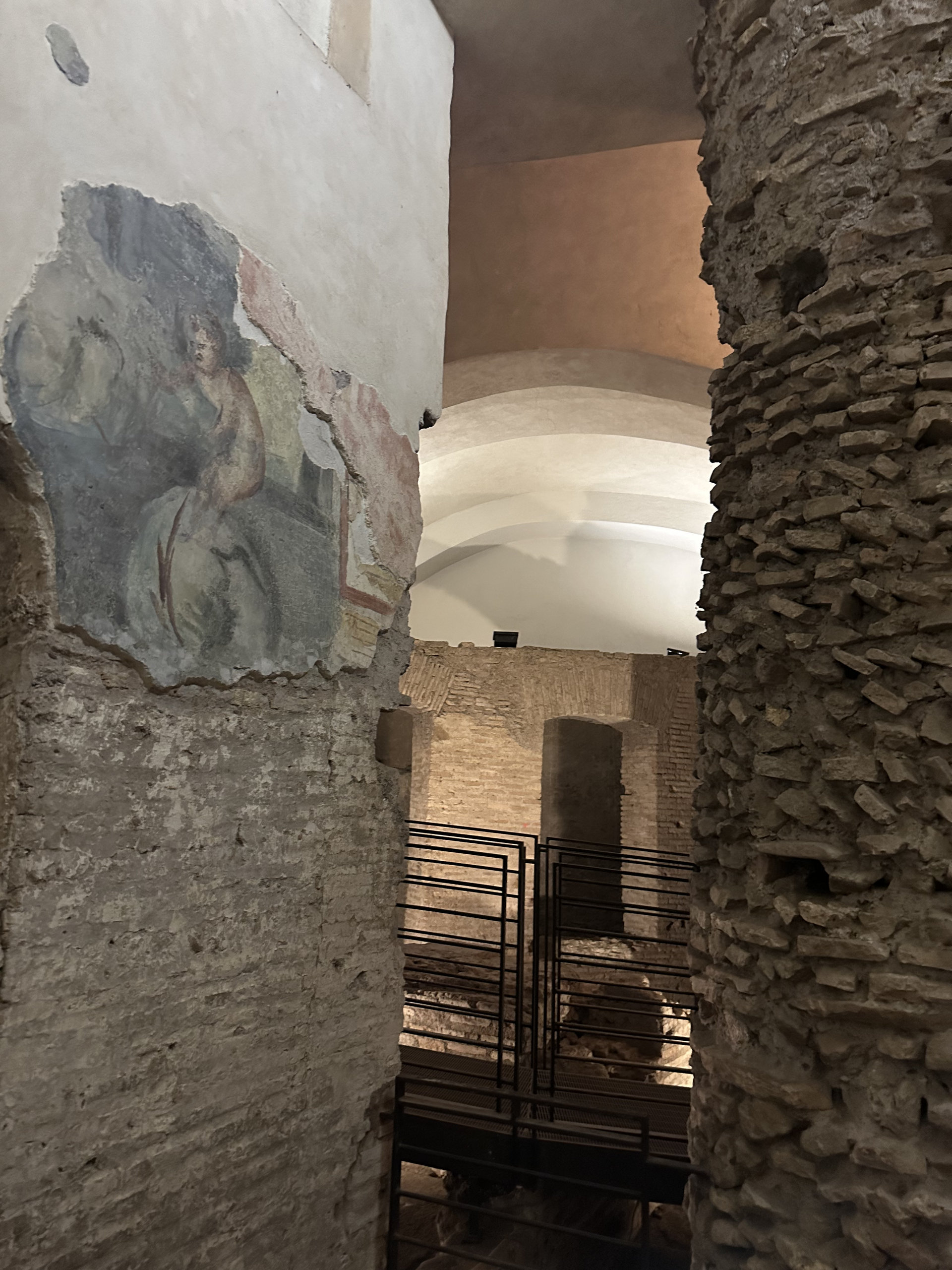 Fragment of a fresco on a plaster-and-brick pillar, with iron railings and vaults beyond