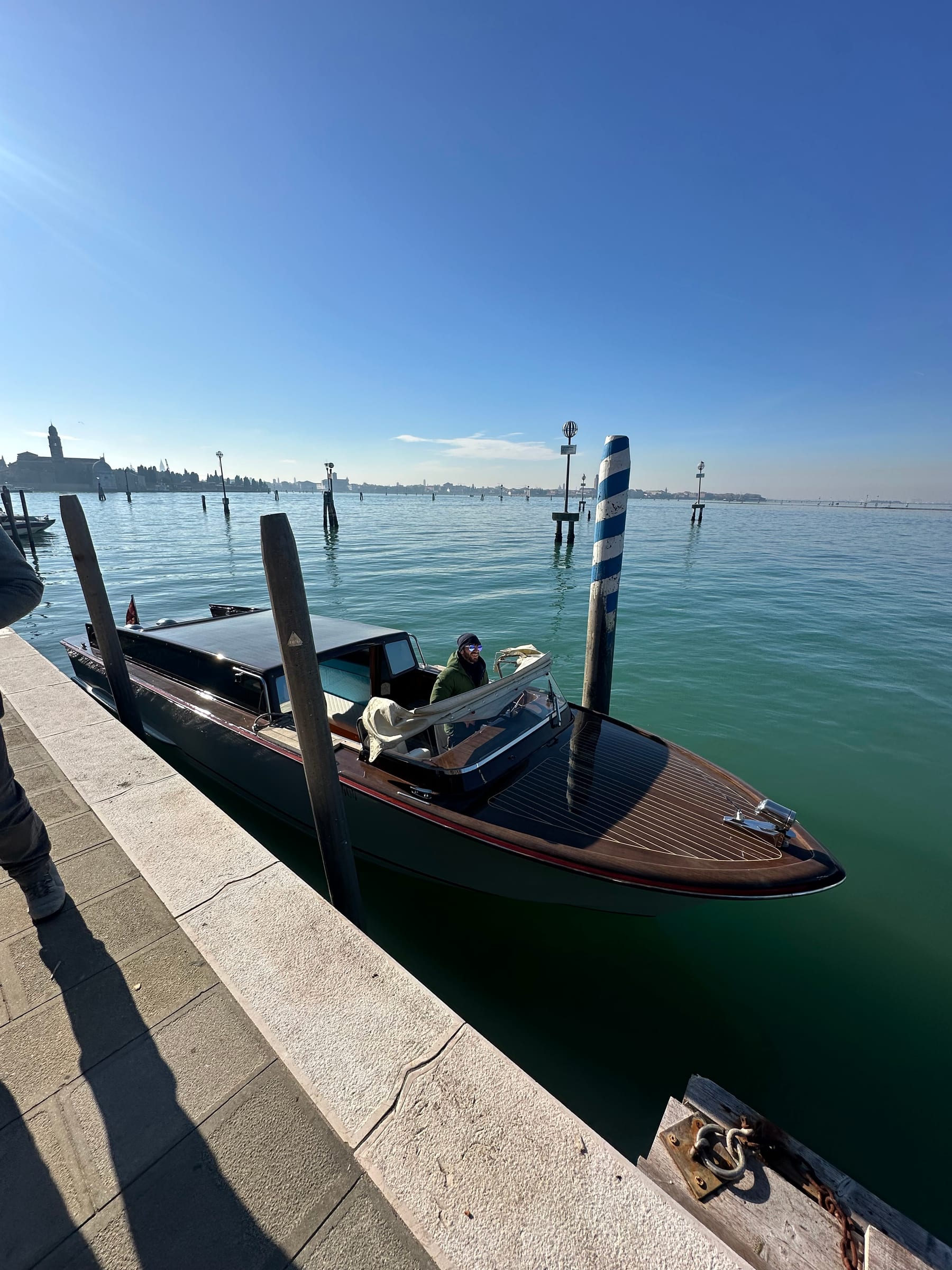 Private wooden water taxi moored at a stone quay on the Venetian lagoon, with its driver at the wheel