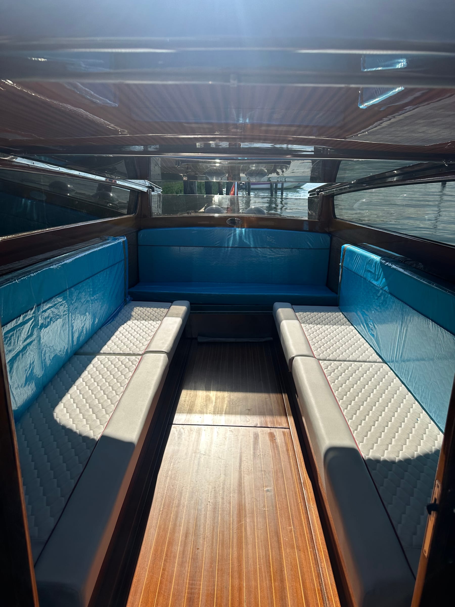 Cabin of a Venetian water taxi with quilted white seats, turquoise cushions and a polished wooden floor